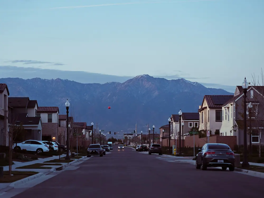 Residential street lined with houses and parked cars, mountains in the distance