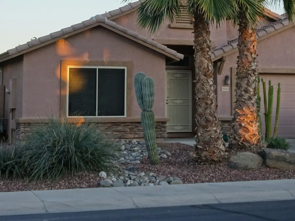 Tan stucco desert home with palm trees, cactus, and gravel landscaping