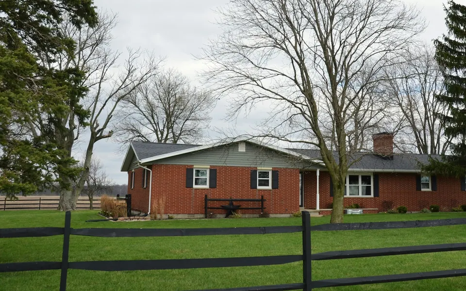Modest single-story brick ranch home behind a wooden rail fence