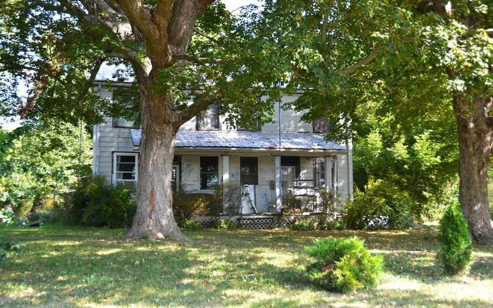 Dated two-story family home with a front porch beneath a large old shade tree