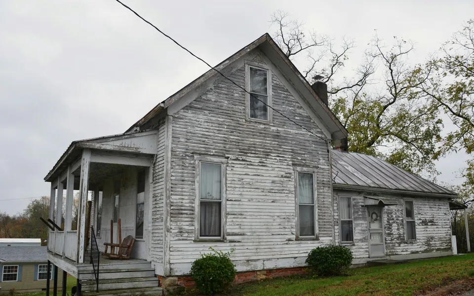 Older white wood-sided house with peeling paint and a worn side porch